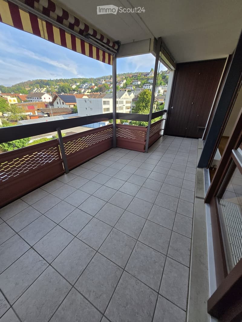 Balcony with tiled floor, wooden railing, and scenic view of a town with houses and greenery.