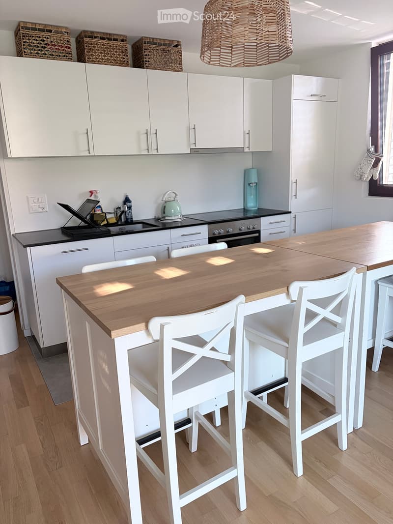 Modern kitchen with white cabinets, a wooden island, white stools, and various appliances including an oven and a faucet.