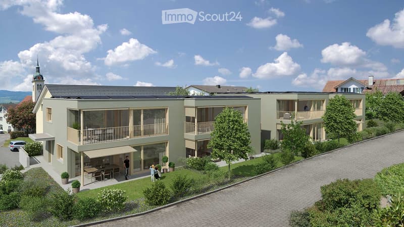 Modern two-story building with balconies, solar panels on the roof, and a small outdoor seating area with a table and chairs.