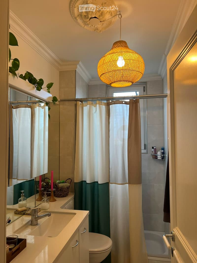 Modern bathroom with a double sink vanity, a toilet, a shower with a curtain, decorative candles, and a woven basket on the counter.