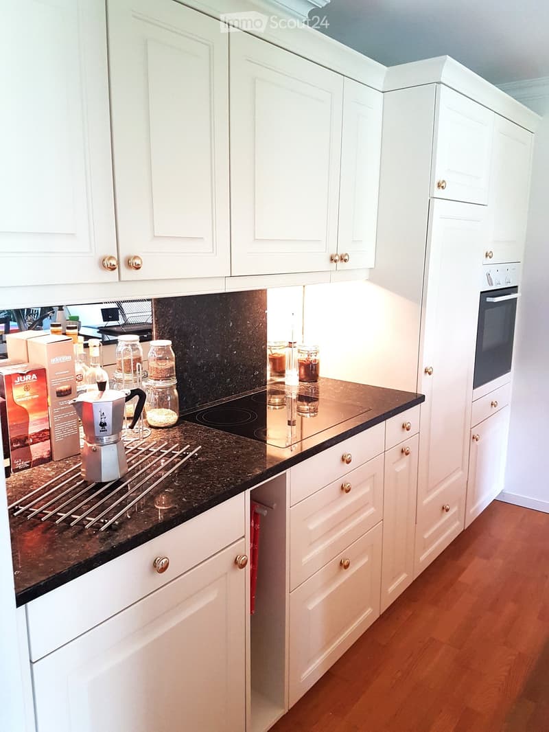 Modern kitchen with white cabinets, dark granite countertop, coffee maker, jars, and an oven.