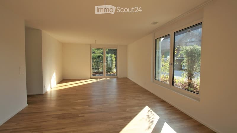 Empty room with wooden flooring, large windows, and a sliding glass door leading to an outdoor area.