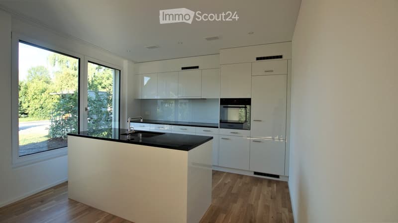 Modern kitchen with white cabinets, black countertop, and a central island. Features a large window with a view of greenery outside.