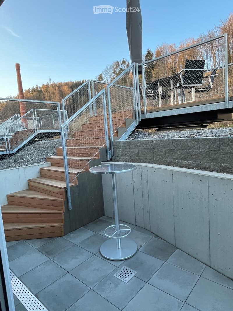 Modern balcony with tiled floor, wooden steps, metal railing, and a round table.