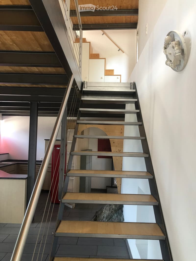 Modern staircase with metal railings and wooden steps, leading to an open area with visible kitchen and storage cabinets.
