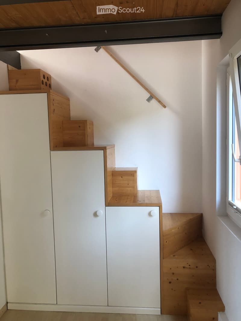 Modern hallway with wooden staircase, white built-in storage cabinets, and a window on the right side.