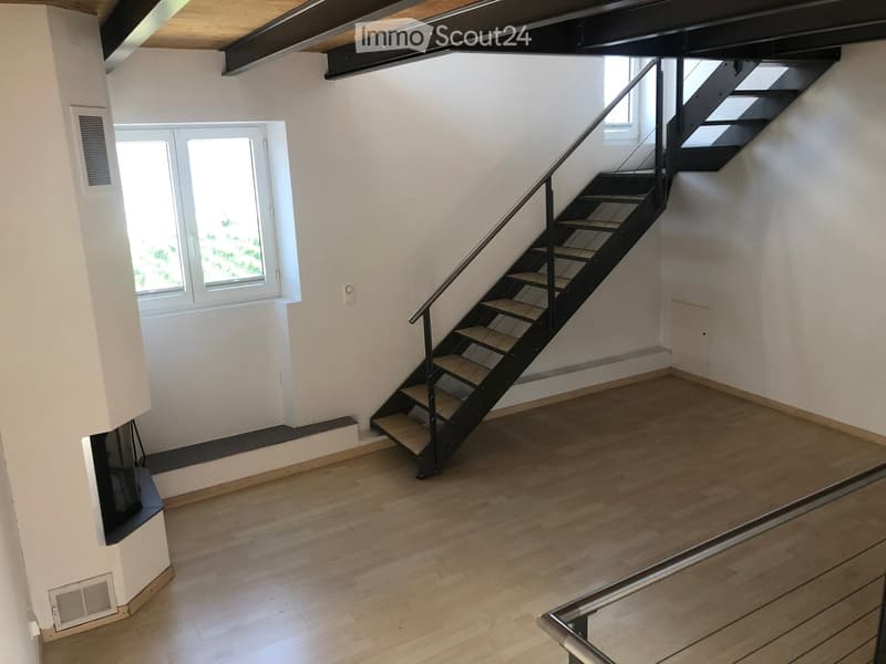 Empty room with wooden flooring, white walls, and a staircase leading upwards. The room has a window and a small landing area.