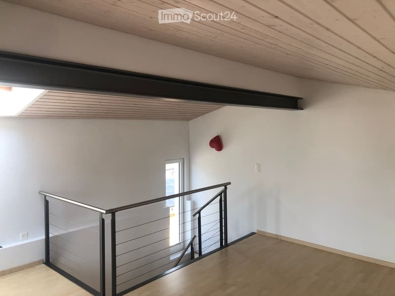 Empty hallway with wooden flooring, white walls, and a modern glass railing leading to a bright room.