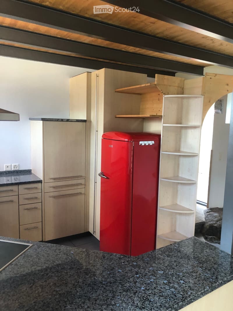 Modern kitchen with light wooden cabinets, a red refrigerator, and a granite countertop.
