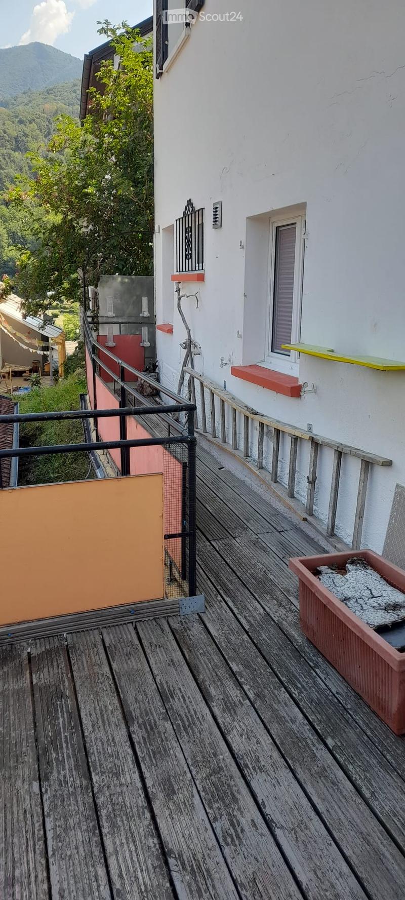 Wooden deck with railing, small planter, and view of greenery and mountains.