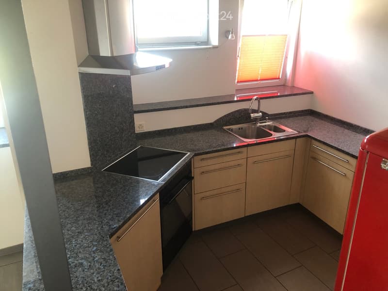 Modern kitchen with granite countertops, stainless steel sink, stove, and light wood cabinets.