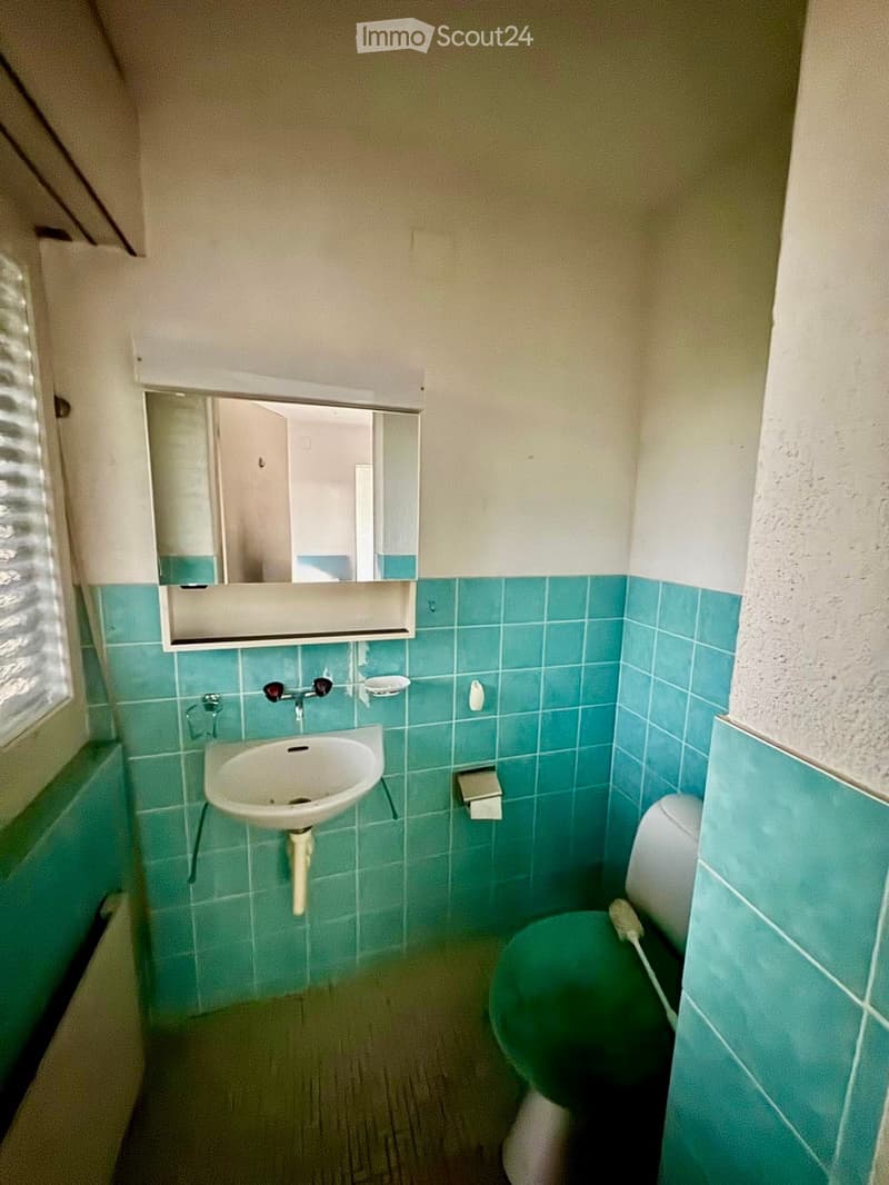 Small bathroom with teal tiles, white sink, toilet, and mirror above the sink.