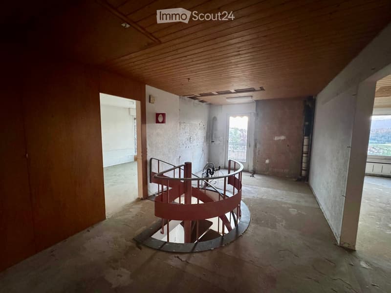 Empty room with a spiral staircase, unfinished walls, and exposed wooden ceiling beams.