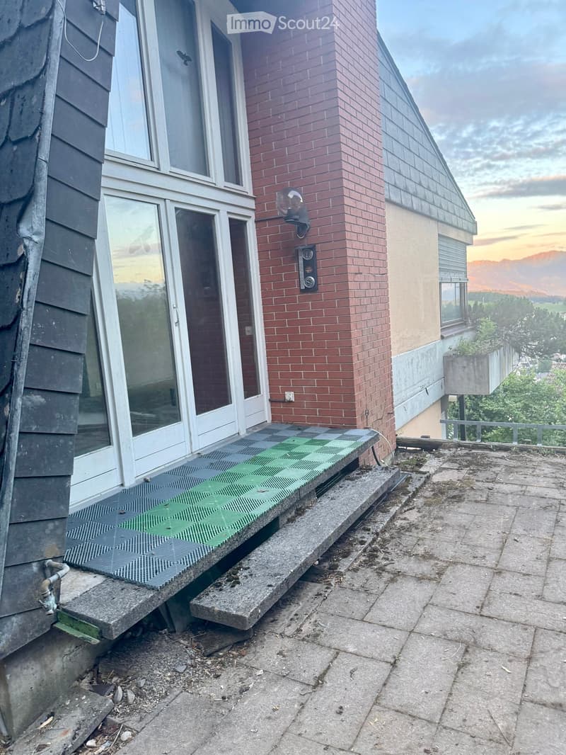Balcony with green protective netting, concrete steps, and a view of surrounding buildings and landscape.