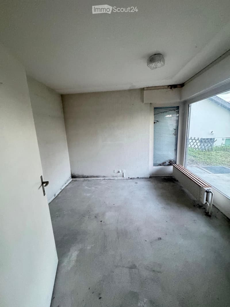 Empty room with concrete floor, white walls, a radiator, a door, and a window with blinds.