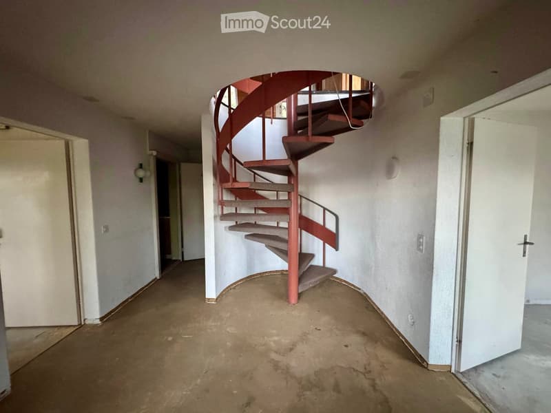 Empty hallway with a spiral staircase leading upwards, unfinished walls, and open doors on either side.