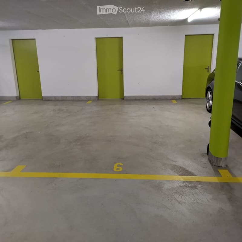 Underground parking area with concrete floors, white walls, green doors, and yellow parking lines.