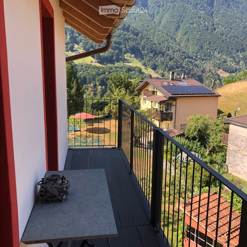 Balcony with a table and a scenic view of a hilly, forested landscape with houses and solar panels.