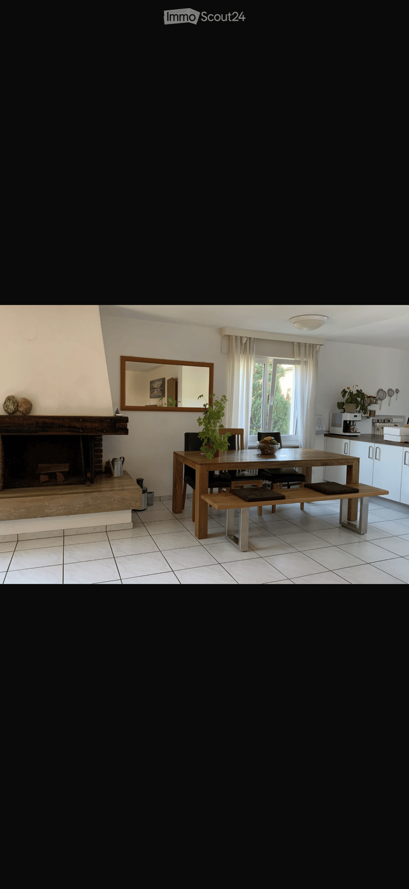 Dining area with a wooden table, bench seating, chairs, fireplace, mirror, and kitchen area with cabinets and counter.