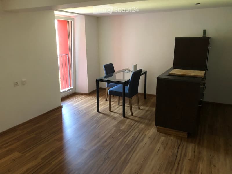 Dining room with wooden floor, glass dining table, two chairs, and a dark wooden cabinet.