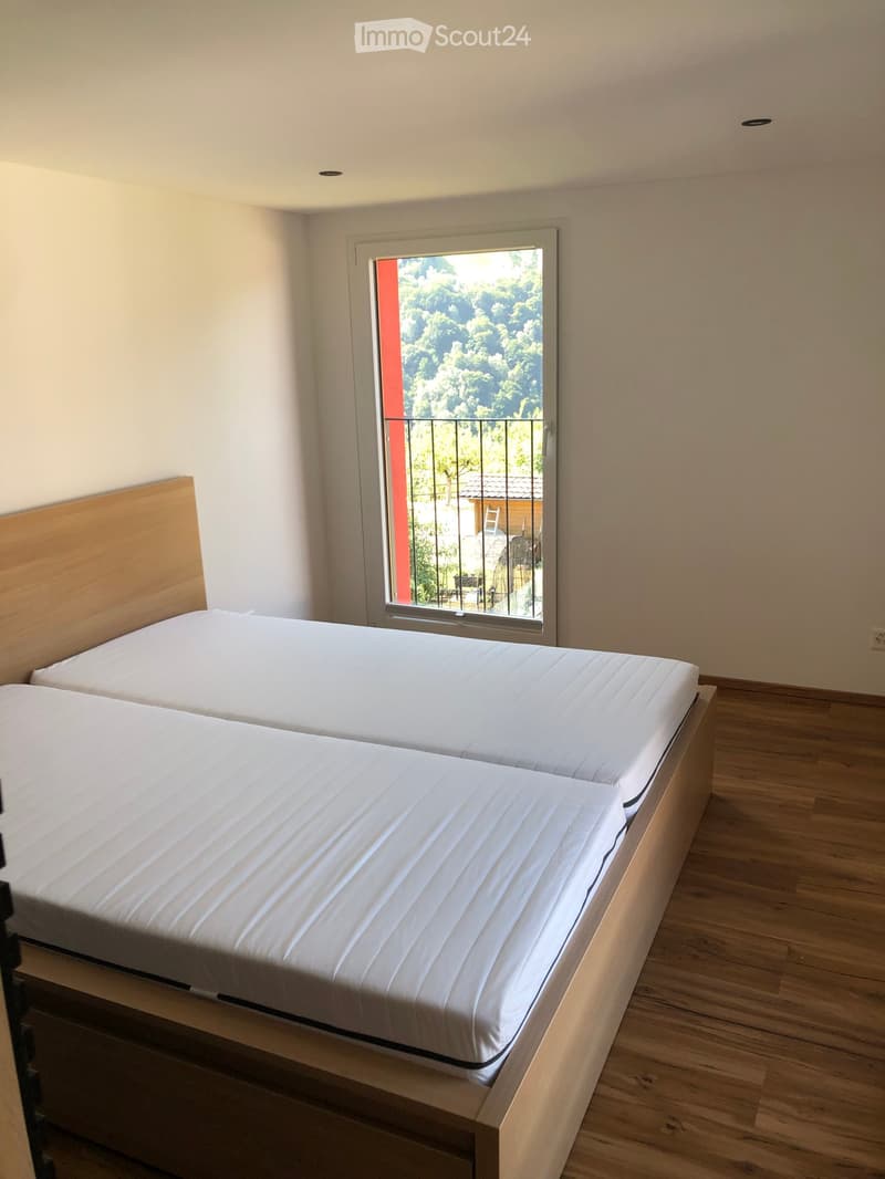 Bright bedroom with two single beds, wooden headboards, and a large window with a view of greenery and a balcony.