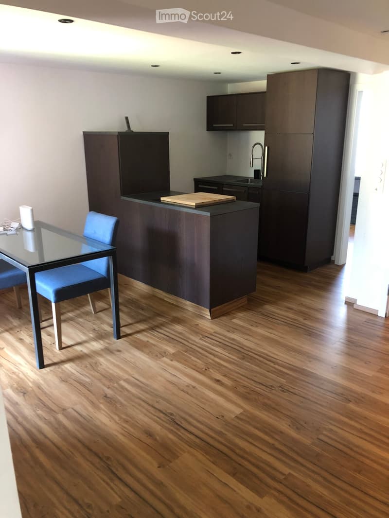 Modern kitchen with dark wood cabinets, a central island, a glass dining table with blue chairs, and a wooden cutting board on the island.