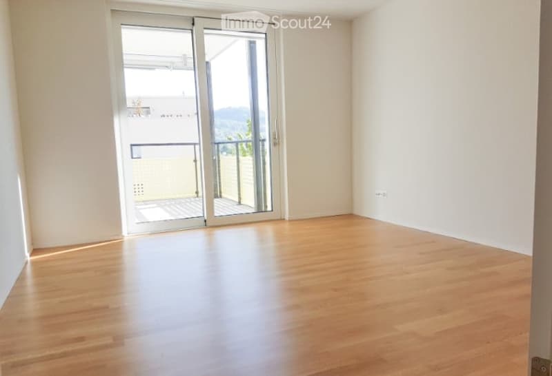 Empty room with wooden flooring and large sliding glass doors leading to a balcony.
