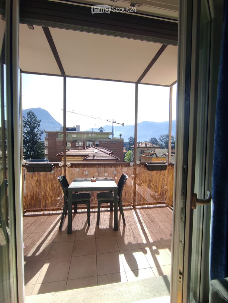 Balcony with a table and two chairs, wooden deck, view of mountains and cityscape.