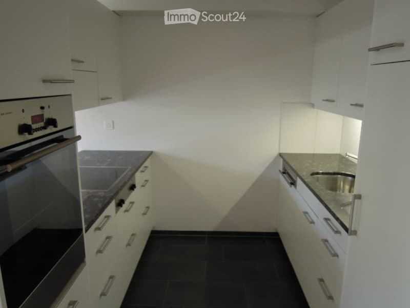 Modern kitchen with white cabinets, black countertops, and a stainless steel sink. Features an oven on the left side and ample storage space.