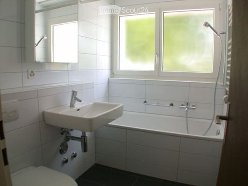 Modern bathroom with white tiles, a sink, bathtub, showerhead, and a mirror above the sink.