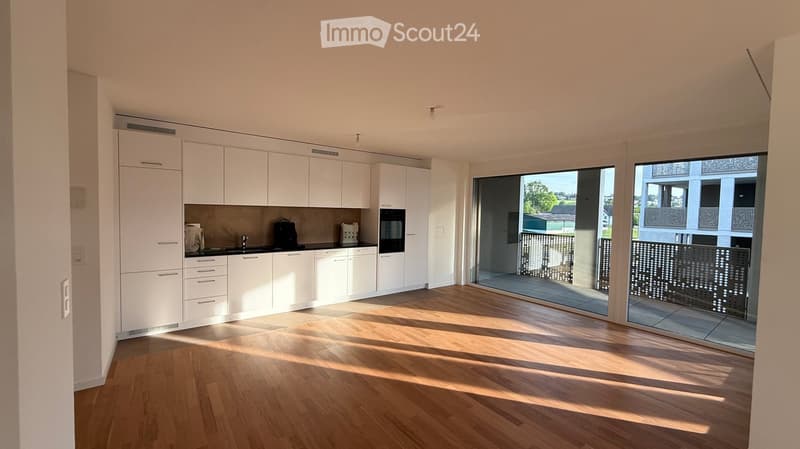 Modern kitchen with white cabinets, wooden flooring, and large windows offering a view of the outdoor area.