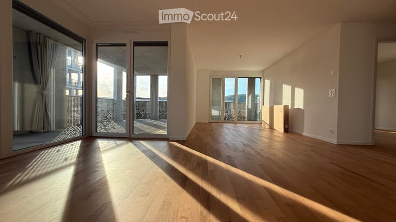 Empty room with wooden flooring, large windows, and sliding glass doors leading to a balcony.