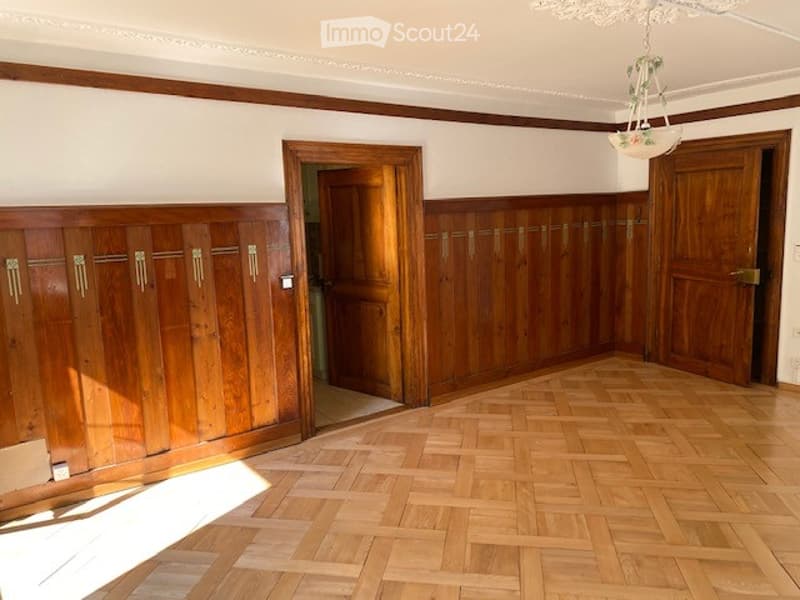 Empty room with wooden panel walls, wooden floor, and two wooden doors.