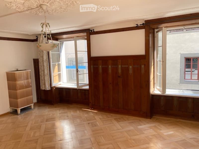 Empty room with wooden flooring, large windows, built-in wooden cabinetry, and a small chest of drawers. No furniture or personal items present.