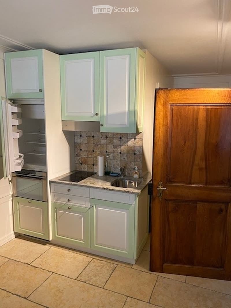 A modern kitchen with light green cabinets, a stainless steel sink, and a built-in oven. The countertop is tiled, and the floor is made of beige tiles.