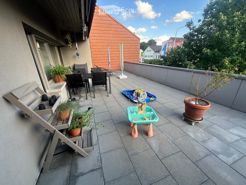 Balcony with tiled floor, outdoor furniture including a table and chairs, potted plants, and children's toys.