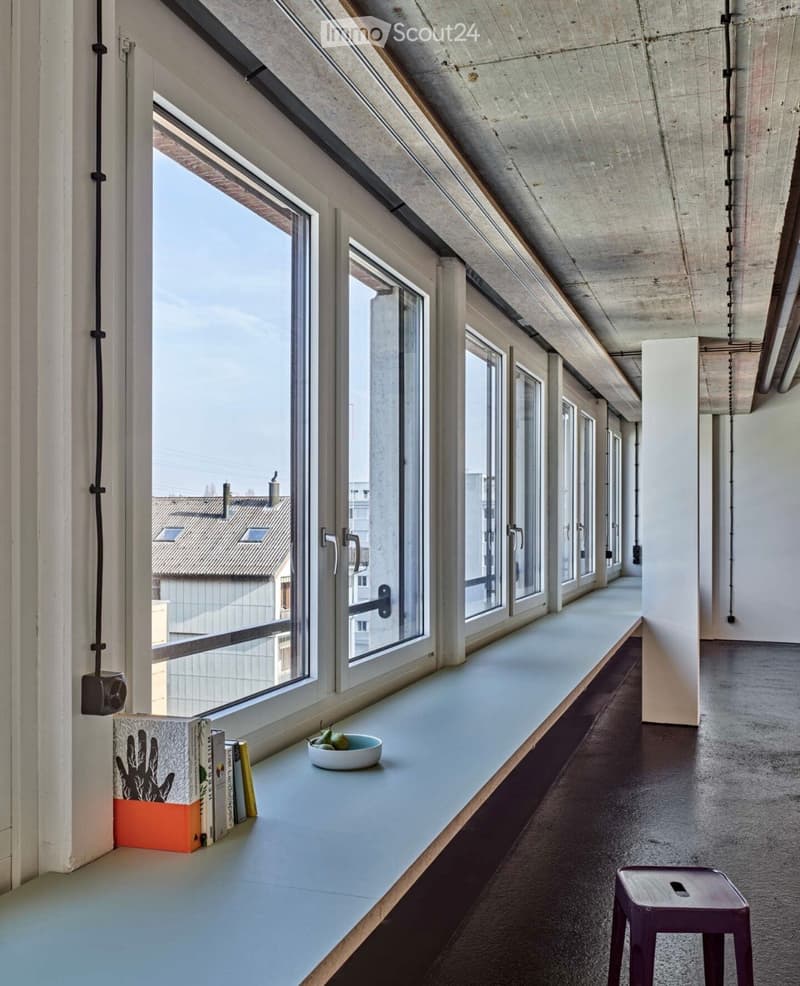 A modern, minimalist hallway with large windows, a long white bench, and a few decorative items including books and a bowl of fruit.