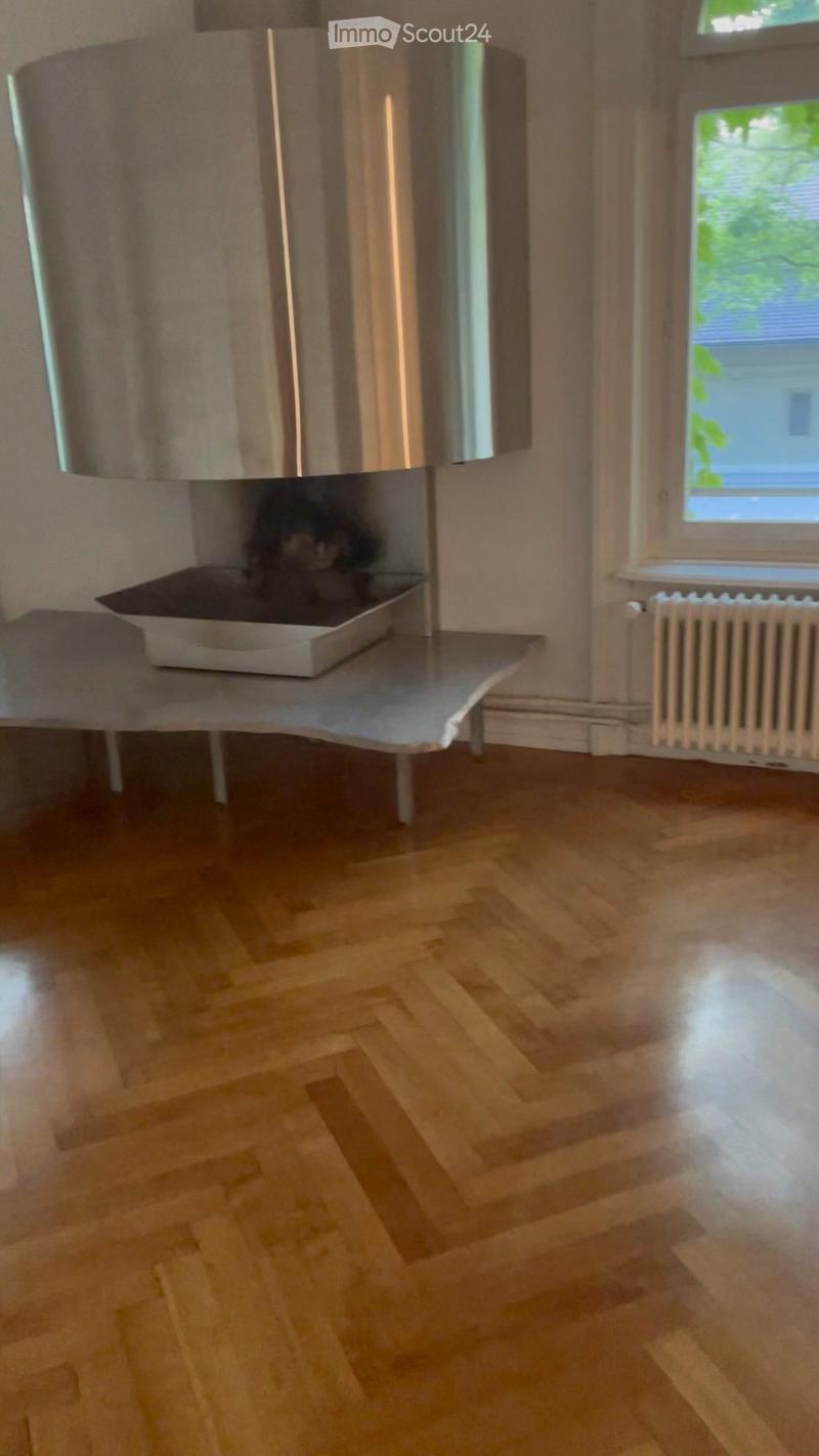 Empty room with wooden flooring, a radiator, and a window with a view of greenery. No furniture or equipment is present.
