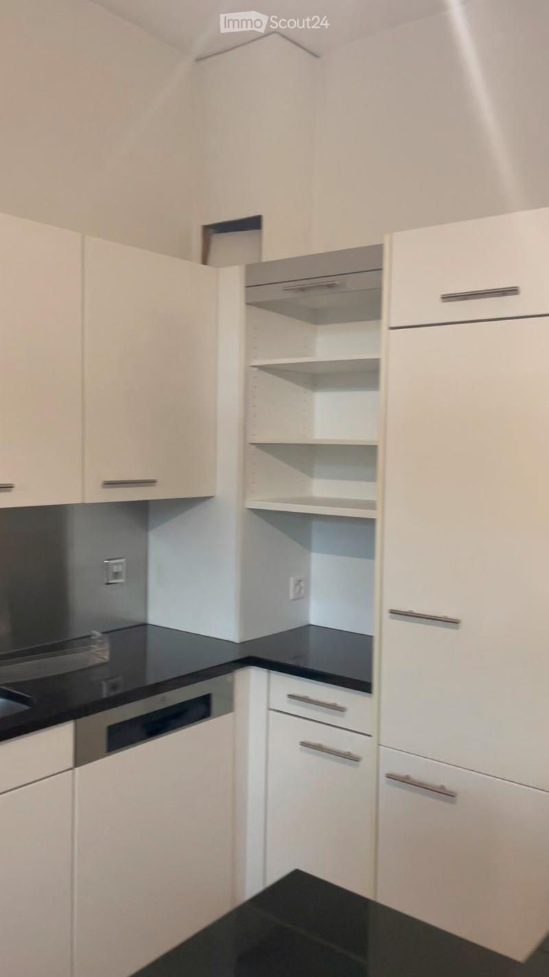 Modern kitchen with white cabinets, black countertops, and stainless steel appliances including an oven and range hood.