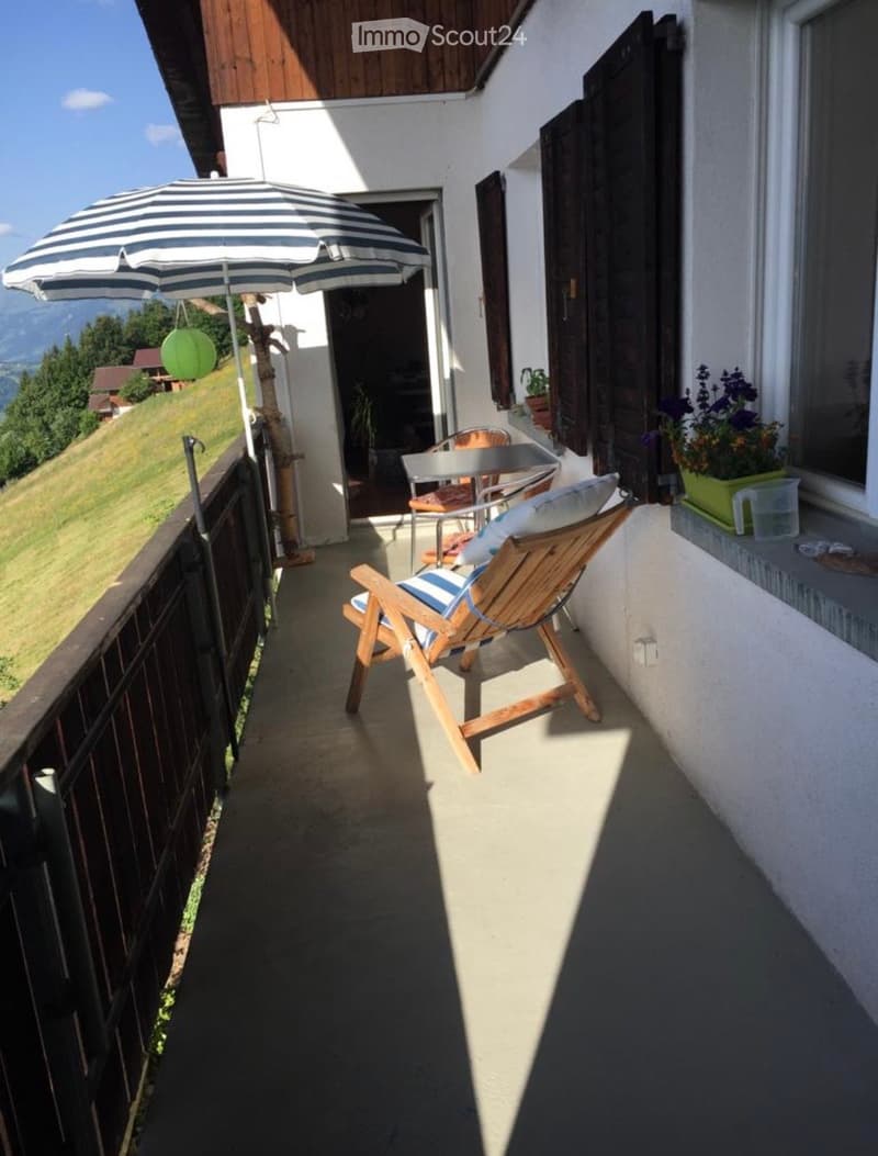 Balcony with a wooden chair, small table, and umbrella, overlooking a scenic landscape.