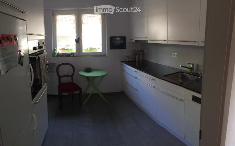 Modern kitchen with white cabinets, stainless steel sink, and a small round table with a chair near the window.