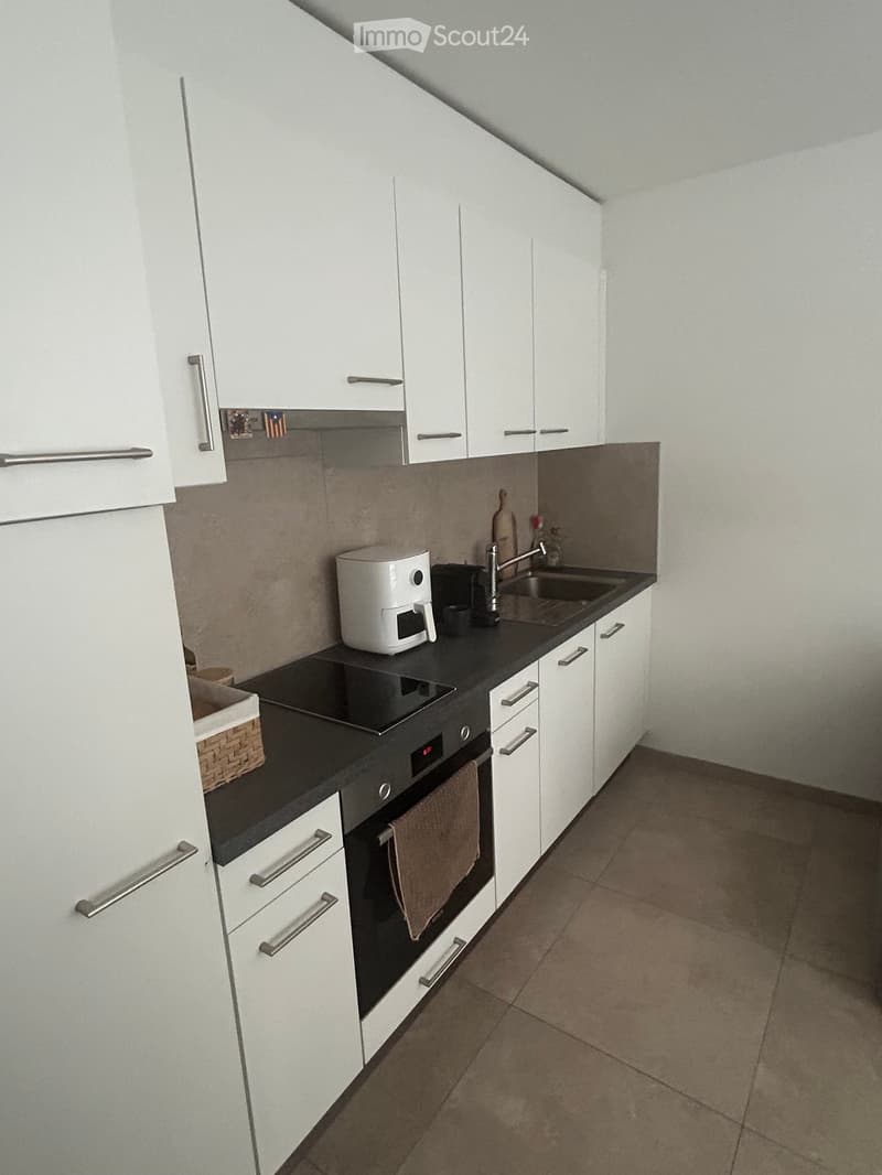 Modern kitchen with white cabinets, black countertops, and stainless steel appliances including an oven, coffee maker, and sink.