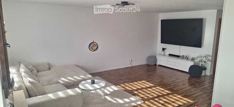 Modern living room with light-colored sofa, white coffee table, flat-screen TV mounted on wall, sideboard with decorative items, and wooden flooring.