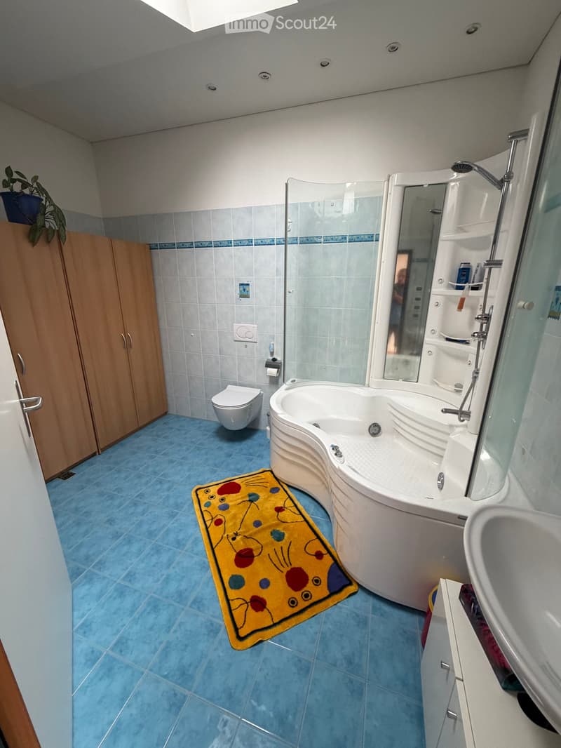 Modern bathroom with blue tiles, a curved bathtub, a toilet, a sink, a mirror, and a colorful rug.