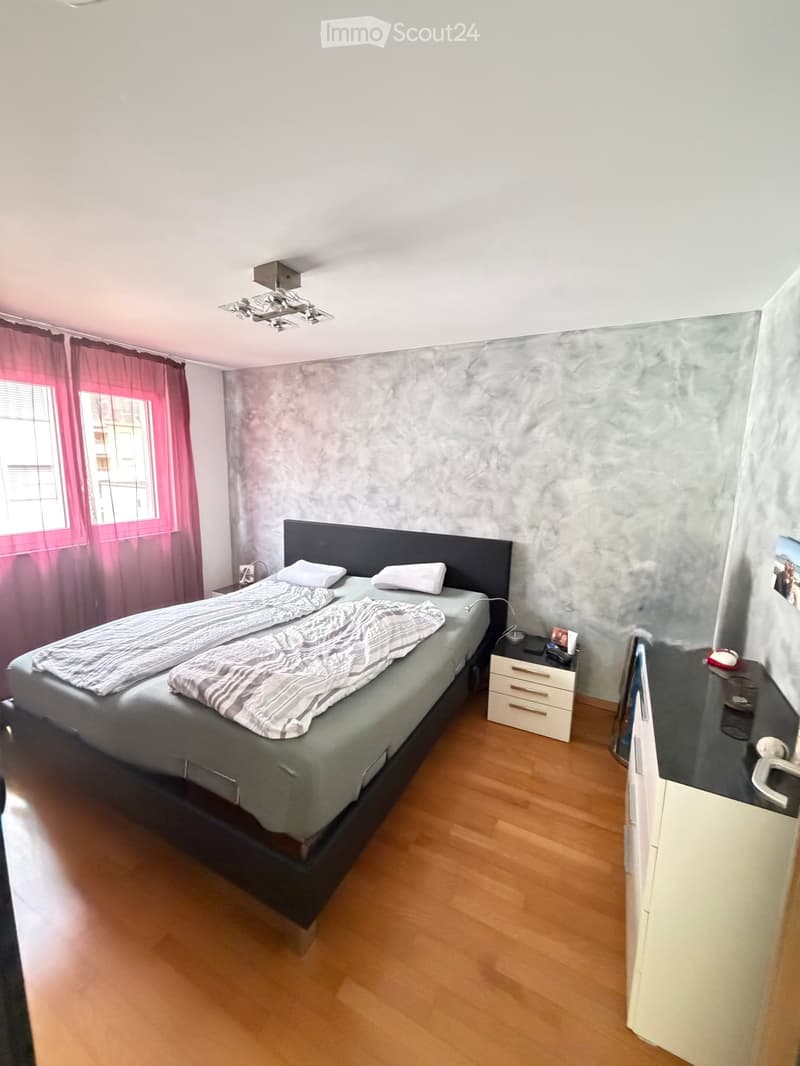 Modern bedroom with a double bed, nightstand, mirror, and wooden flooring.