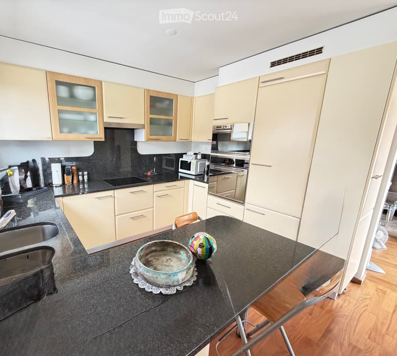 Modern kitchen with light-colored cabinets, stainless steel appliances, and a dark granite countertop. A small table with a bowl and a colorful ball is placed on the counter.