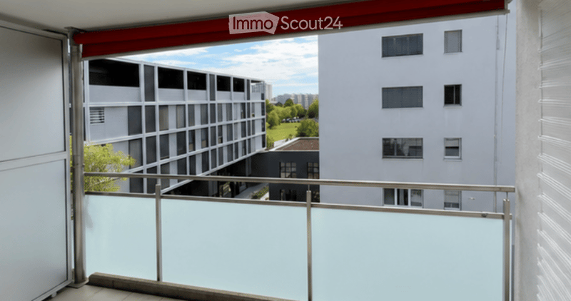 Balcony with a modern metal railing, overlooking a cityscape with contemporary buildings and greenery.
