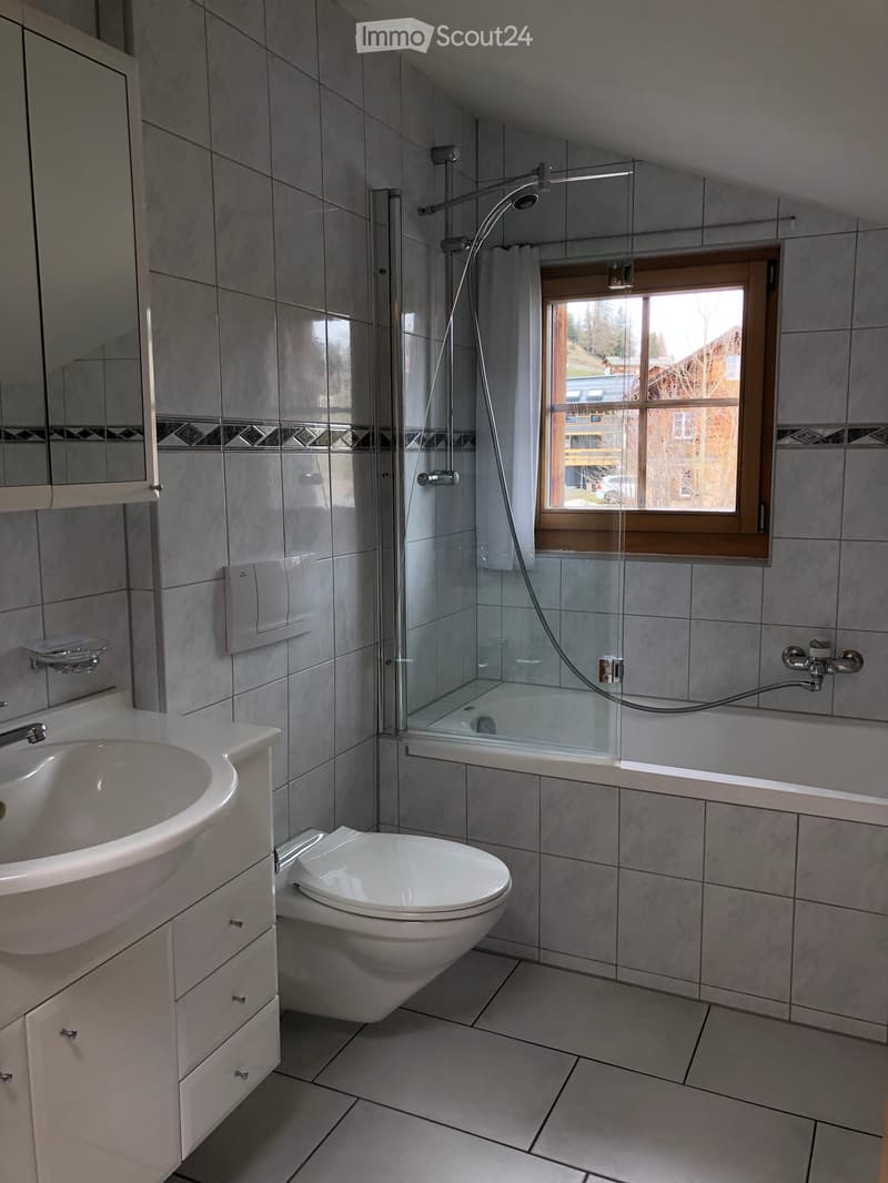 Modern bathroom with a white sink, toilet, glass-enclosed shower, and a window offering a view of the outdoors.