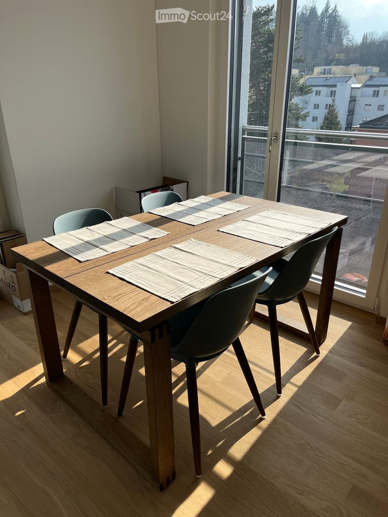 Dining area with a wooden table, four chairs, and a view of the balcony and cityscape.