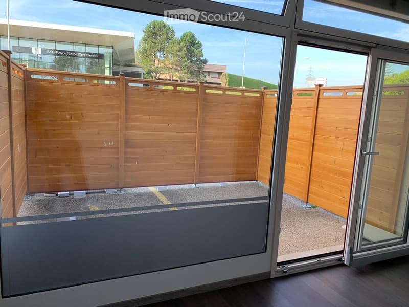 Balcony with wooden fence, sliding glass doors, and view of outdoor area with trees and buildings.